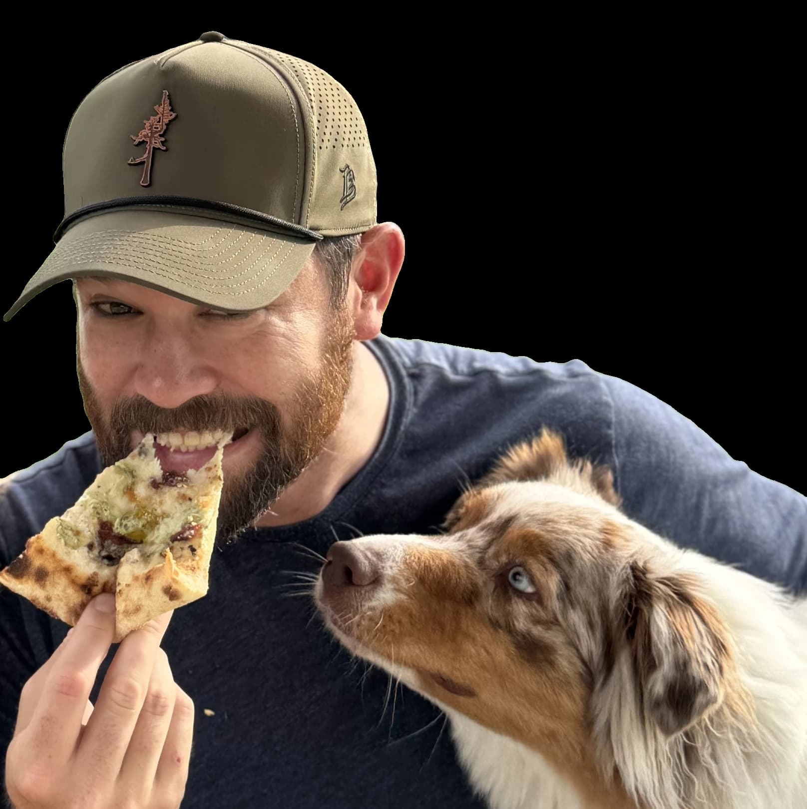 Thomas smiling with a slice of pizza while a dog watches the slice closely.