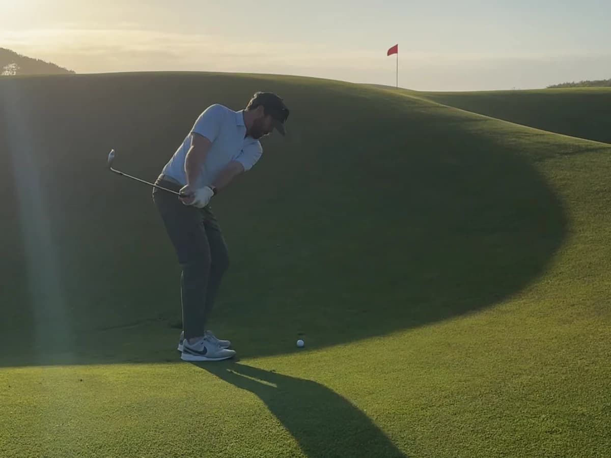 Thomas hitting a golf shot from a deep hollow toward a red flag in evening light.
